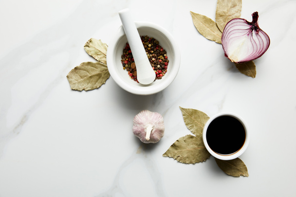 Vista superior de granos de pimienta, salsa de soja con cebolla y ajo sobre hojas de laurel sobre fondo de mármol
 - Foto, imagen
