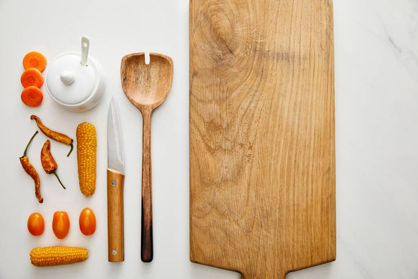 Bovenaanzicht van keukengerei met snijplank en groenten op marmeren ondergrond - Foto, afbeelding