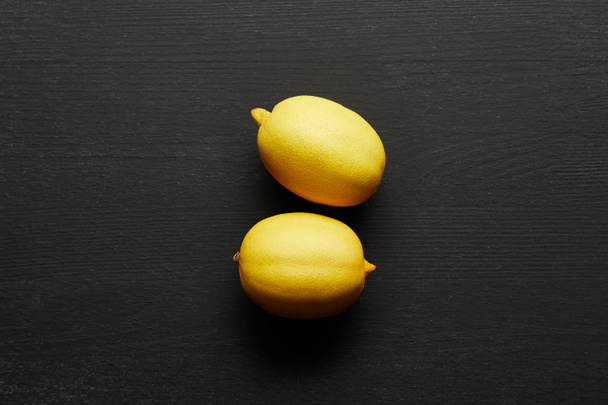 Draufsicht auf zwei frische Zitronen auf schwarzem Holzhintergrund - Foto, Bild