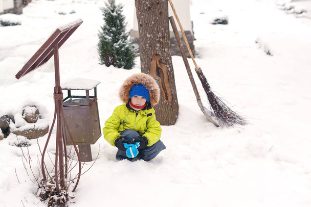 Kid plays with snow in back yard. Child makes snowballs. Happy childhood - Photo, Image