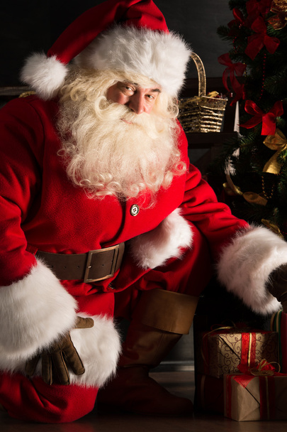 Santa placing gifts under Christmas tree in dark room - Zdjęcie, obraz