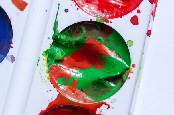Een vlek van rode verf in een blik groene verf. Een palet van verf - Foto, afbeelding