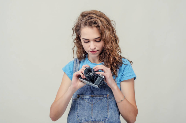Kudrnatá brunetka v džínových montérkách drží v rukou filmovou kameru, kroutí pákami. - Fotografie, Obrázek