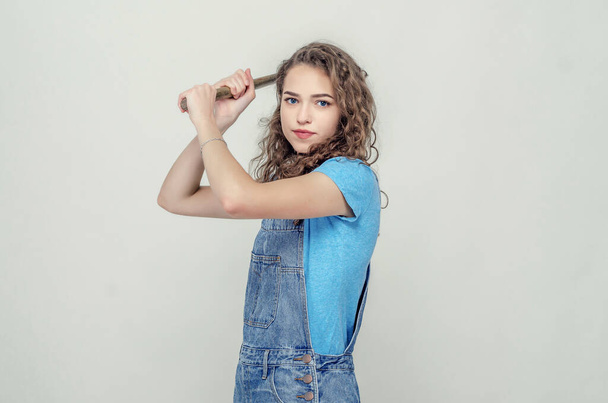 Curly cheerful brunette girl in denim overalls holds a hammer in - Zdjęcie, obraz