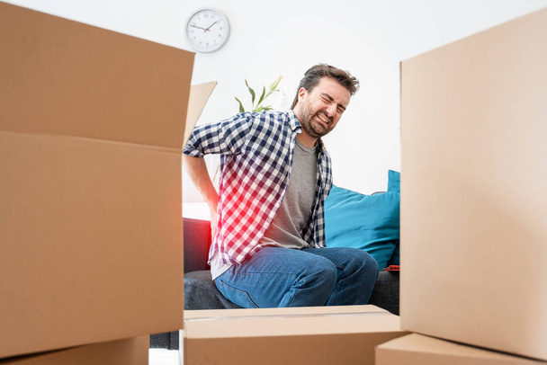 Man moving boxes and feeling back pain because heavy weight - Fotoğraf, Görsel