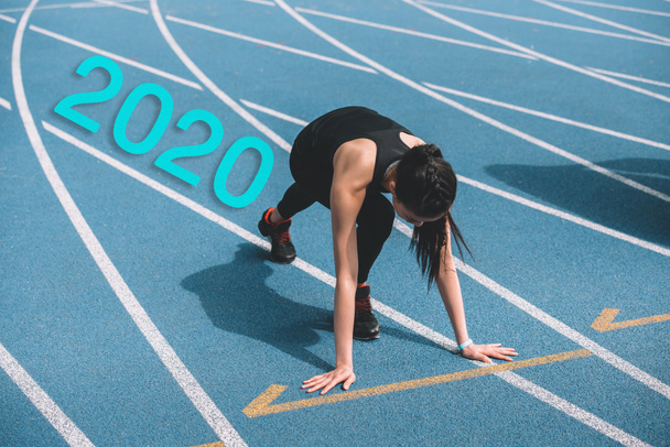 young sportswoman standing in start positing on running track near 2020 lettering - Photo, Image