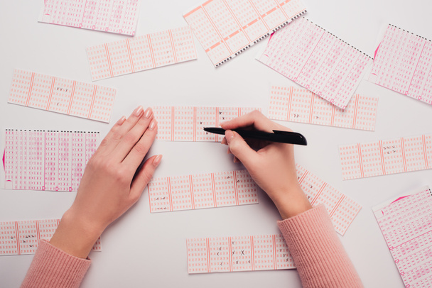 partial view of woman marking numbers on lottery tickets on white table - Photo, Image