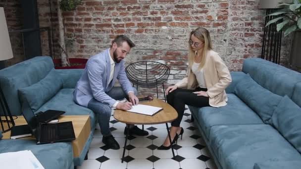 Handsome bearded businessman and blond charming businesswoman signing the business agreement and after shaking hands each other in modern office - Footage, Video