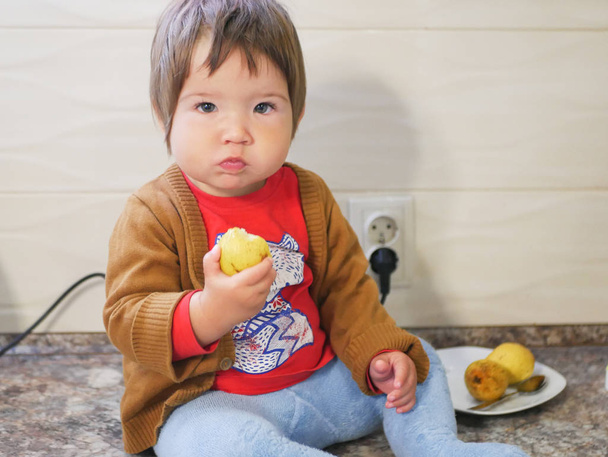 маленька дитина їсть грушу. хлопчик їсть фрукти на високому стеку. на кухні
. - Фото, зображення