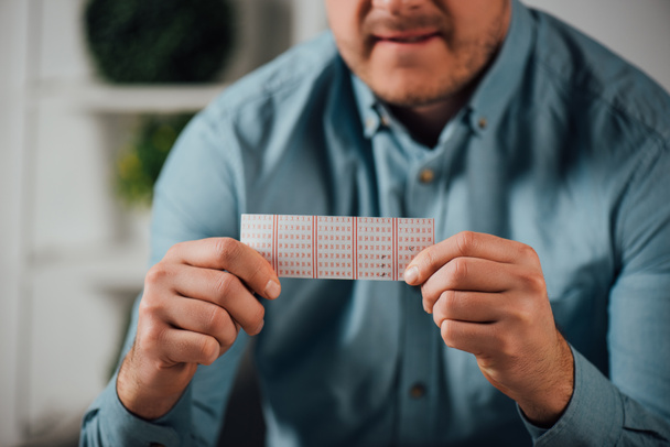 vista recortada del hombre preocupado sosteniendo billete de lotería mientras espera los resultados de la lotería
 - Foto, Imagen