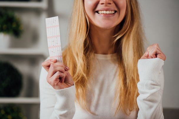 corte vista da mulher mostrando gesto vencedor enquanto segurando bilhete de loteria
 - Foto, Imagem