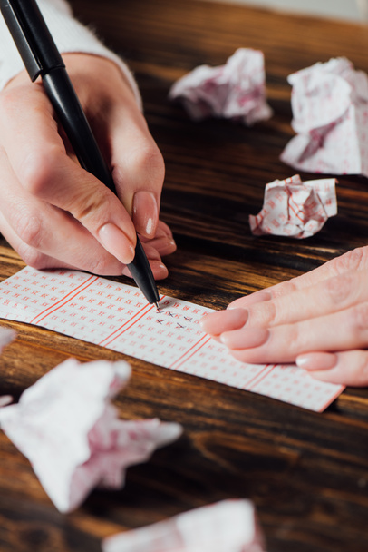 visão parcial dos números de marcação do jogador no bilhete de loteria perto de cartões de loteria amassados na mesa de madeira
 - Foto, Imagem