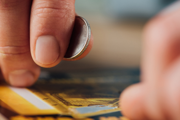 vista de cerca de la moneda de plata en la mano del jugador cerca de billete de lotería rayado
 - Foto, Imagen