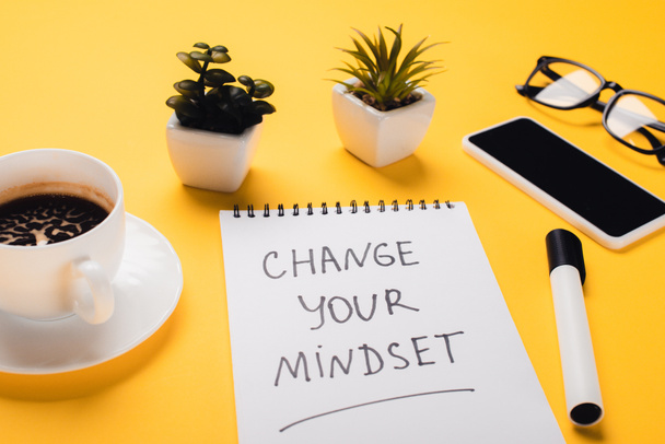 notebook with change your mindset inscription near coffee cup, potted plants, felt-tip pen, smartphone and glasses on yellow desk - Photo, Image