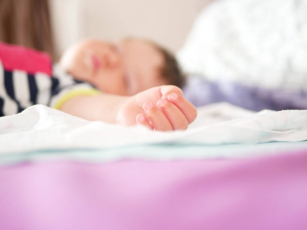 ребенок спит в кровати родителей. руки протянули спокойный сон ребенка. крупным планом. ребенок 0-1 лет. очаровательный прекрасный ребенок спит спокойно в постели, имеет приятный здоровый сладкий сон, заботятся. От воздействия
 - Фото, изображение
