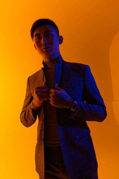 Portrait of a young asian man standing over yellow background. Fashion asian man - 写真・画像