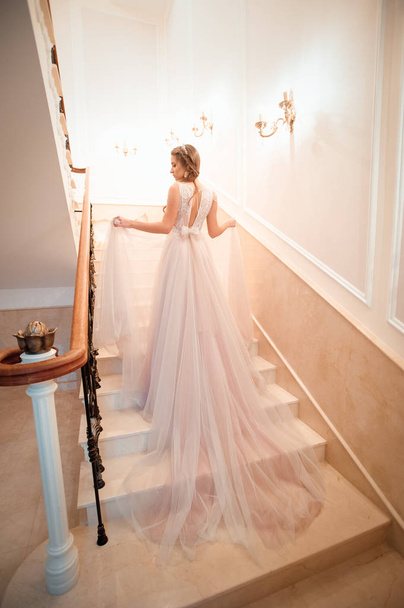 Een meisje in een trouwjurk loopt de trap op. Een beige jurk. Mooie dame in luxe balzaal jurk loopt de trap op van haar paleis. Balusterleuning aan beide kanten. Vintage concept - Foto, afbeelding