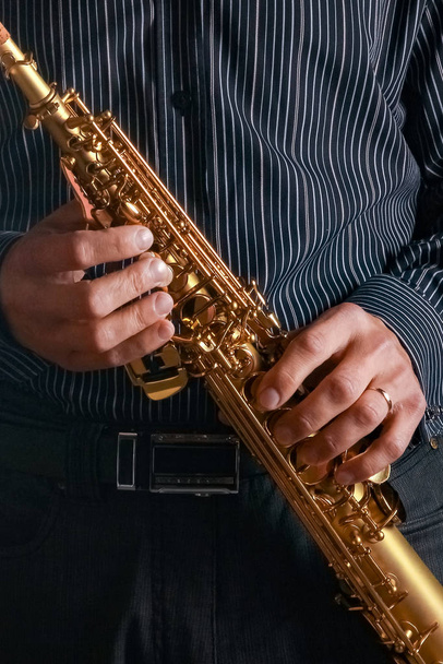 soprano saxophone in the hands of a guy on a black background - Φωτογραφία, εικόνα