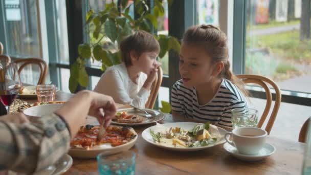 Mädchen spricht mit Mutter, die die Pizza schneidet und ein Stück davon in den Teller legt - Filmmaterial, Video
