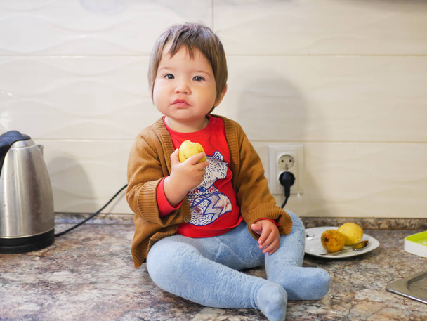 маленька дитина їсть грушу. хлопчик їсть фрукти на високому стеку. на кухні
. - Фото, зображення