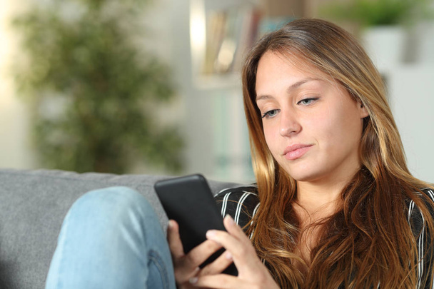 Serious woman using mobile phone on a sofa at home - Photo, Image