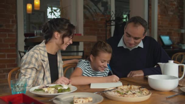 Family lunch, parents help thier daughter to write something - Materiał filmowy, wideo