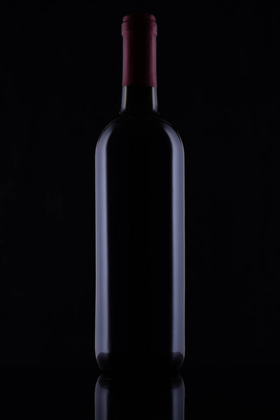 Black glass bottle of red wine on black background - Φωτογραφία, εικόνα