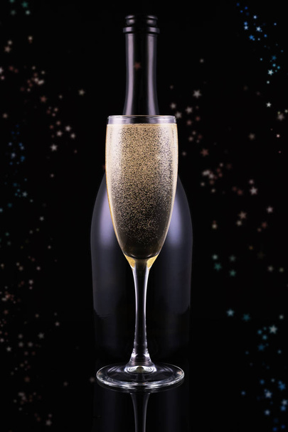 Botella y copa de champán sobre fondo negro con círculos bokeh dorados. Lugar para el texto. Concepto festivo
. - Foto, imagen