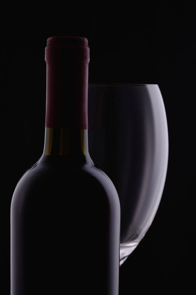 Bicchiere di vino rosso e una bottiglia di vino con riflessi su sfondo nero
 - Foto, immagini