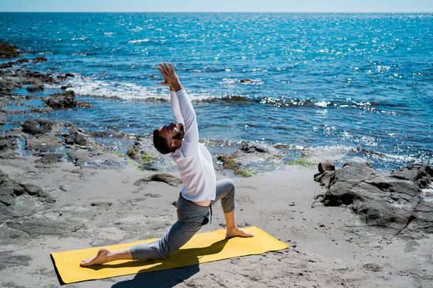 Athletic biały człowiek robi ćwiczenia jogi w pobliżu morza. - Zdjęcie, obraz