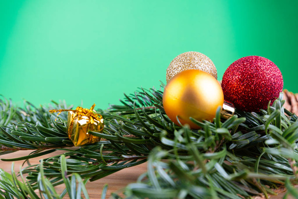 コピースペース付きの緑の背景の前に木製のテーブルの上にクリスマスオーナメント(クリスマスの泡、キャンディーの杖、プレゼント)と緑のモミの枝 - 写真・画像