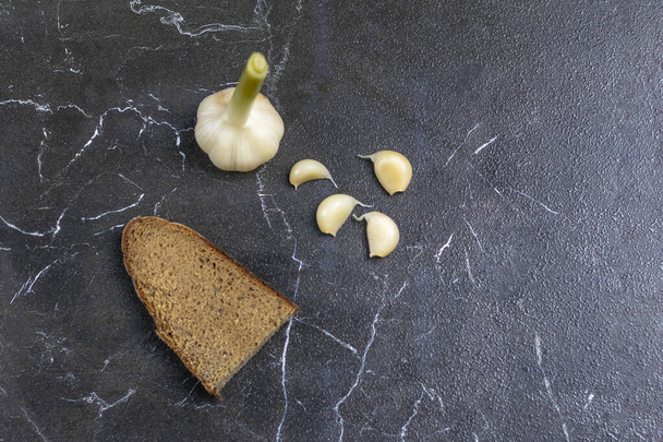 garlic soaked in a special sauce. next to a piece of dark rye bread. close-up. on marble background - Photo, Image