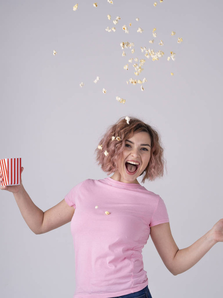 A young woman in a pink t-shirt smiling and throwing up popcorn in the air - Foto, Bild