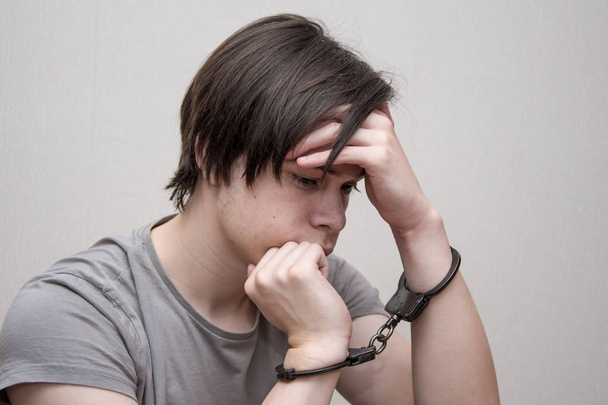 Ein gefesselter Teenager sitzt auf einem grauen Hintergrund. Jugendstraftäter, Jugendstrafrecht. Mitglieder krimineller Jugendgruppen und Banden. - Foto, Bild