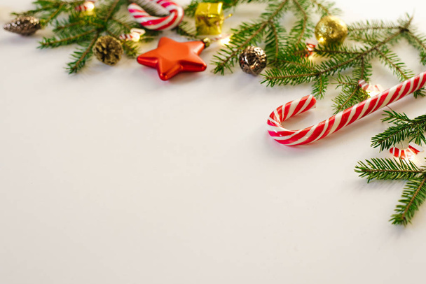 Marco de Navidad de ramas de abeto y juguetes de árbol de Navidad de oro y marrón, bastones de caramelo de menta y luces ardientes sobre fondo blanco, espacio para copiar. Tarjeta de felicitación de año nuevo
 - Foto, imagen