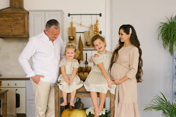 Krásná přátelská rodina se dvěma dcerami šťastná a usmívající se ve své kuchyni čeká na nového člena rodiny. Těhotná máma - Fotografie, Obrázek