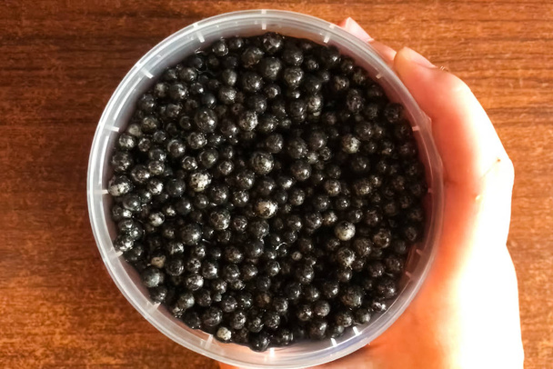 Zwarte kaviaar in plastic container op tafel. Heerlijke kaviaar - Foto, afbeelding