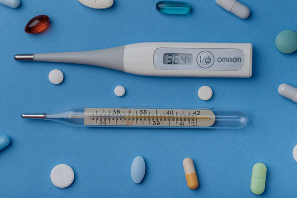 thermometer onder pillen en munten op een blauwe achtergrond - Foto, afbeelding