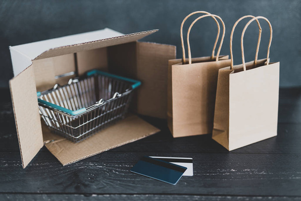 online shopping, parcel with shopping basket and bags next to it - Φωτογραφία, εικόνα