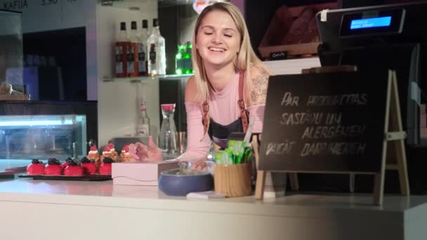 Schattige meisje verkoper lacht leunend op de toonbank in de banketbakker - Video