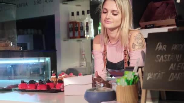 Gyönyörű fiatal lány eladó mutatja ínycsiklandozó sütemények áll a pult mögött - Felvétel, videó