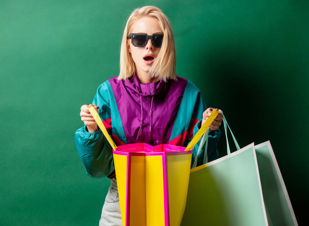 Blonde girl in 90s style jacket with shopping bags on green back - Photo, Image