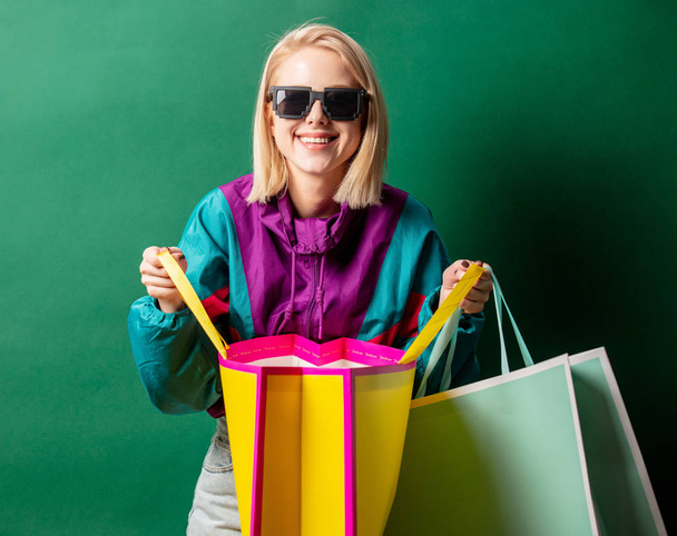 Chica rubia en la chaqueta de estilo 90 con bolsas de compras en la espalda verde
 - Foto, imagen