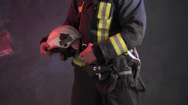 Detailní pohled na statečného hasiče ve speciální uniformě drží ochrannou přilbu stojící u šedé stěny - Záběry, video
