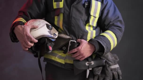 Closeup view of a brave firefighter in special uniform holds protective helmet standing against a gray wall - Footage, Video