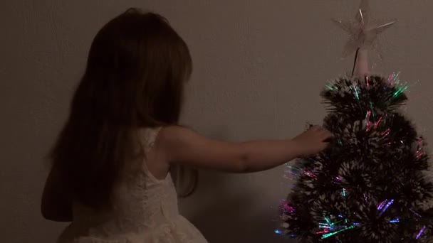 Odada parlak bir çelenk ve yıldızla süslenmiş çok renkli bir yılbaşı ağacı var. Çocuklar ve yetişkinler için tatil. Yeni yıl. Noel ağacı, mutlu tatiller. Noel arşivi. - Video, Çekim