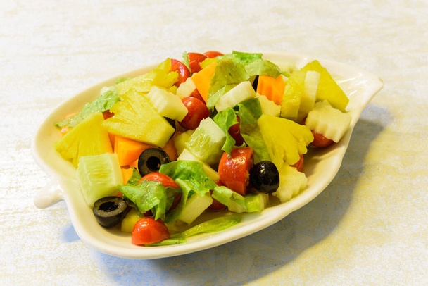 Plat frais de salade mixte de fruits biologiques avec ananas, concombre, pomme, tomates cerises, laitue, carotte, olive. Fibre colorée et saine en forme de feuille blanche plaque
. - Photo, image