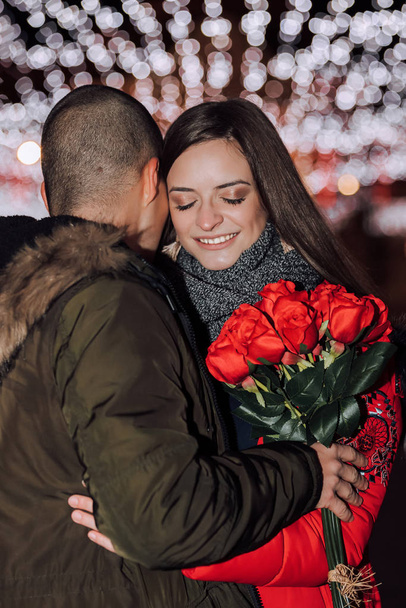 Μια γυναίκα κρατάει ένα μπουκέτο τριαντάφυλλα και χαμογελά αγκαλιάζοντας τον - Φωτογραφία, εικόνα