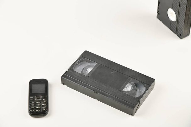 Retro objektumok fehér háttérrel. nyomógombos telefon és videokazetta. A múlt analóg médiatechnológiája. Fénymásolási hely - Fotó, kép