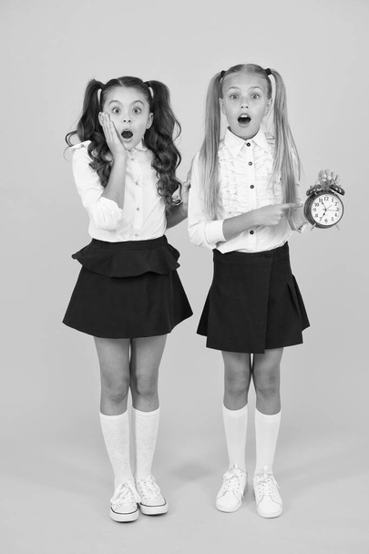 OMG. Got a surprise. Surprised schoolgirls checking time on yellow background. Shocked little children having mouth open with surprise being late. Back to school surprise. Surprise concept - Foto, Bild